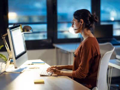 Beautiful business woman working with computer while talking with earphone sitting in the office.